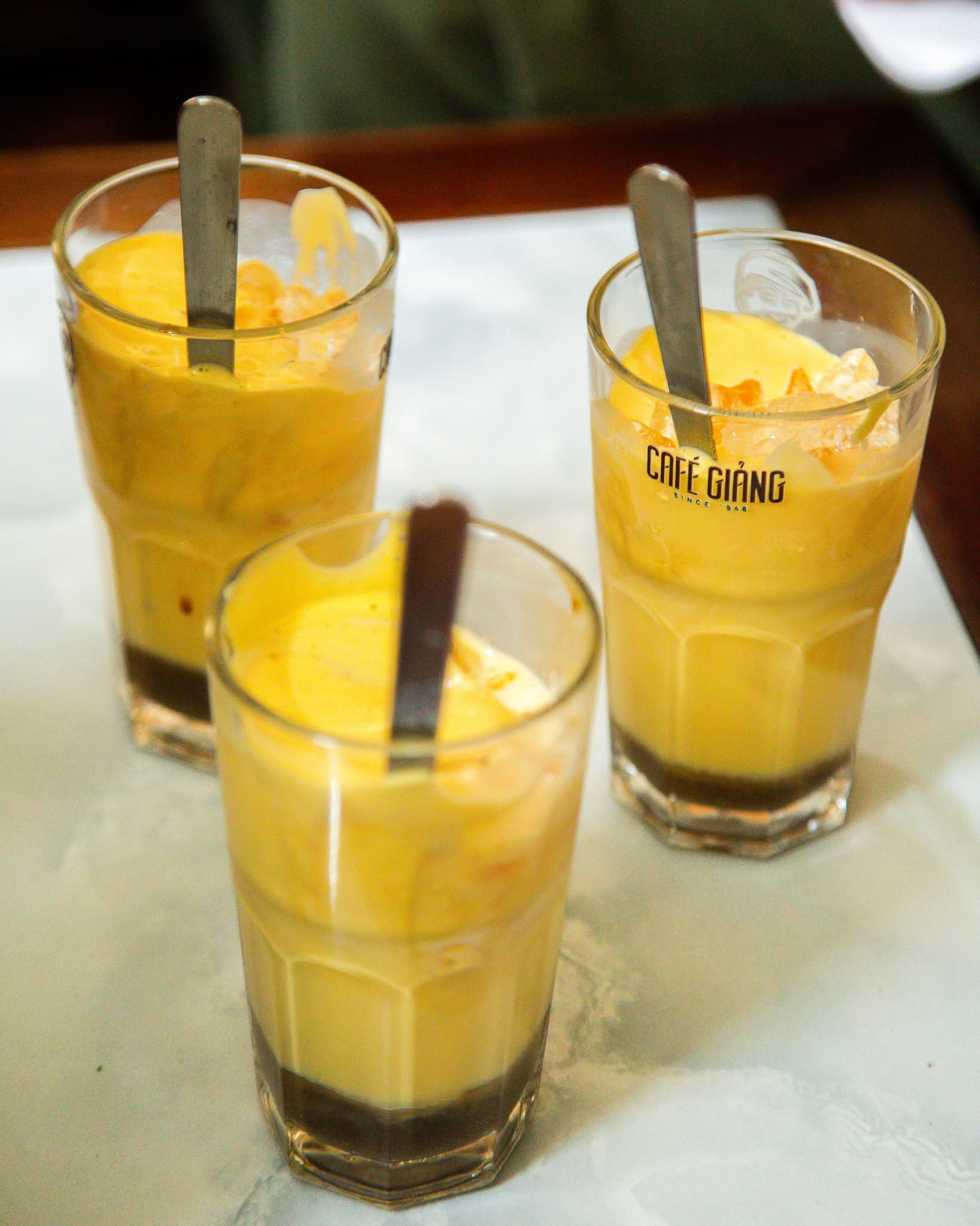 Three glasses of creamy iced Vietnamese coffee served with spoons.